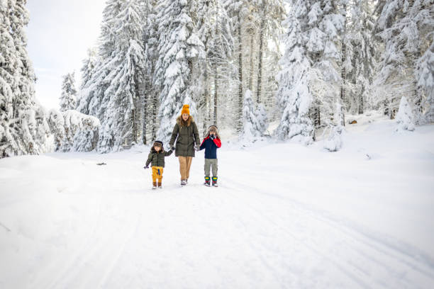 A mother and her two boys take in the beauty of a snowy mountain, walking together on a fresh air.