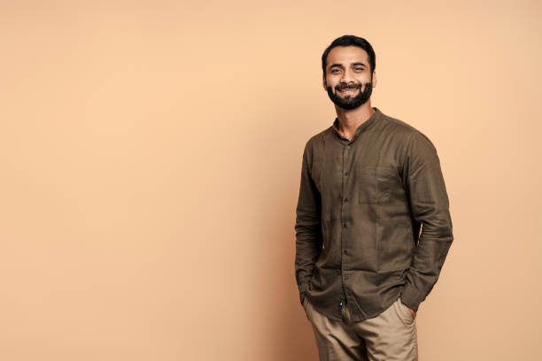 istock Smiling Indian man with hands in pockets looking at camera on beige background 2177197105