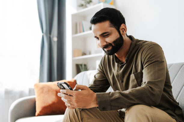 istock Happy, smiling Indian man using smartphone browsing social media at home on sofa 2177197111