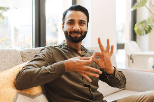 istock Smiling indian man is sitting on sofa and showing sign language gesture looking at camera 2177197196