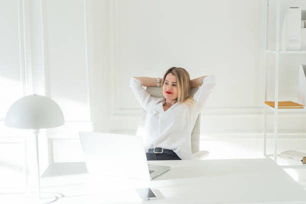 istock Delighted young blonde woman sitting at white table in blouse using laptop 2177199533