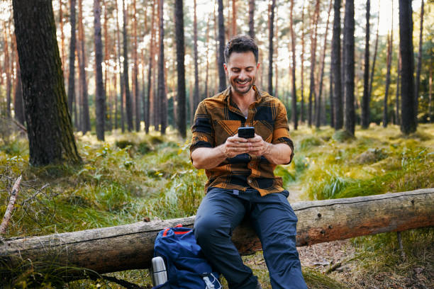 istock Happy man using mobile phone sitting in forest during weekend hike trip 2177199543