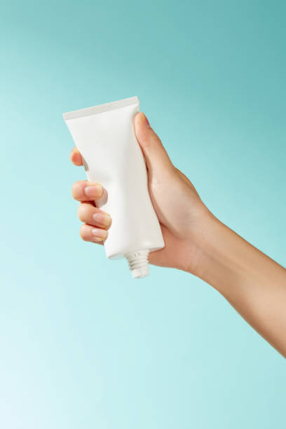 istock A hand gently grasping an unmarked white tube devoid of a stopper against a blue backdrop infuses the picture with an element of freshness, making it appropriate for a skincare promotion. 2177200649