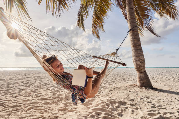 istock Smiling woman reading a book in hammock on the beach. 2177203948