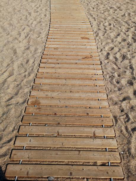 Wooden walkway leading through sandy beach towards the shore on a sunny day for easy access and enjoyment