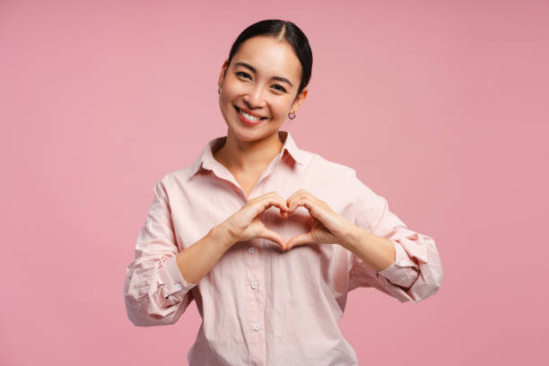 istock Smiling Asian woman making heart shape with hands looking at camera isolated on pink background 2177206528