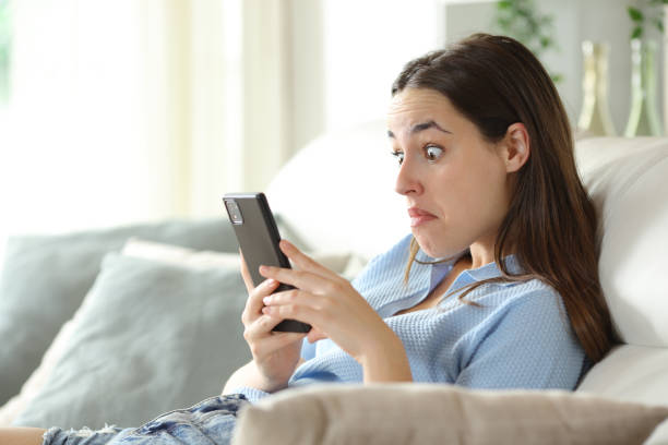 Perplexed woman checking phone on a couch stock photo