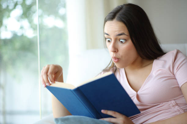 istock Amazed woman reading a paper book sitting in a sofa 2177207026