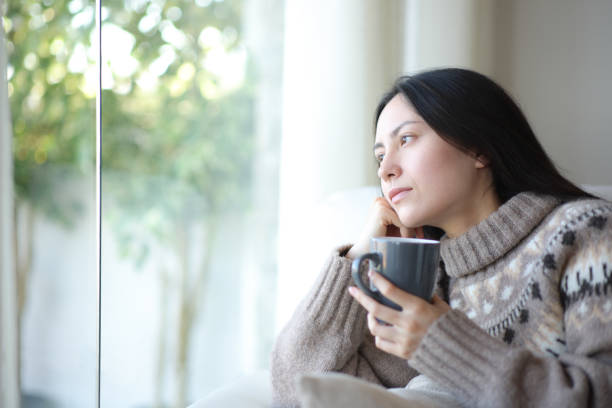 istock Pensive asian woman in winter drinking and looking through a window 2177207036