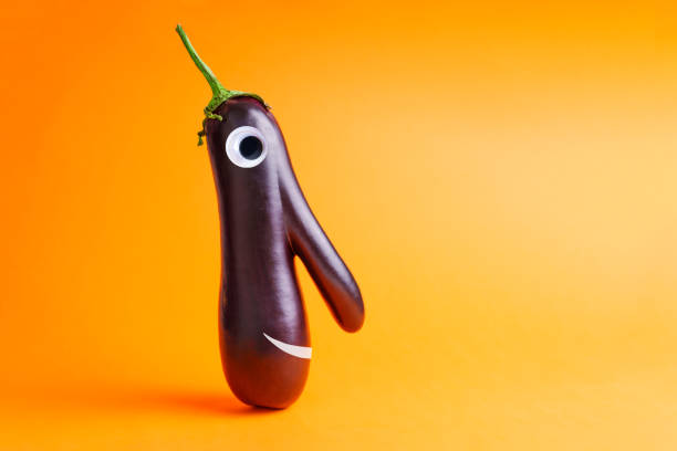 Close-Up Of Hand Holding Eggplant With Anthropomorphic Smiley Face Against Pink Background