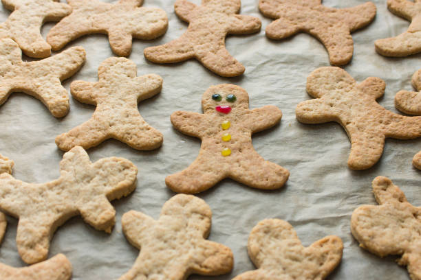 Gingerbread man cookies on baking tray. The only one decorated cookie with smile and eyes. Christmas cookies background. Homemade biscuits. Individuality concept. Cinnamon cookies on baking paper.