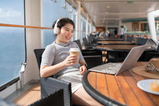 Asia female using laptop working online remotely working from cruise deck while listening music from wireless headphone,freelance asian female woman working online using laptop