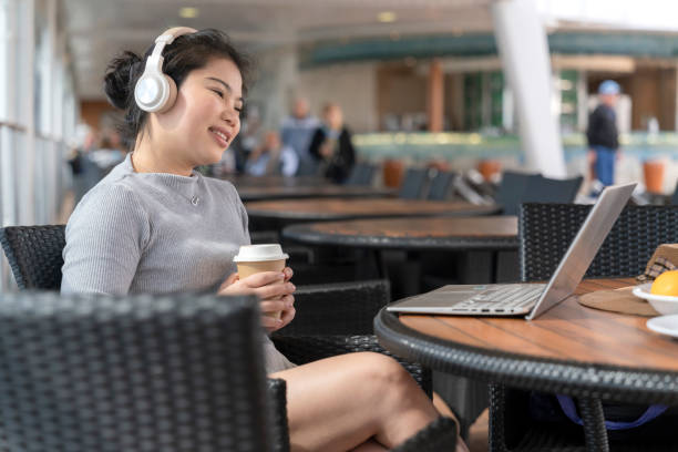 Asia female using laptop working online remotely working from cruise deck while listening music from wireless headphone,freelance asian female woman working online using laptop