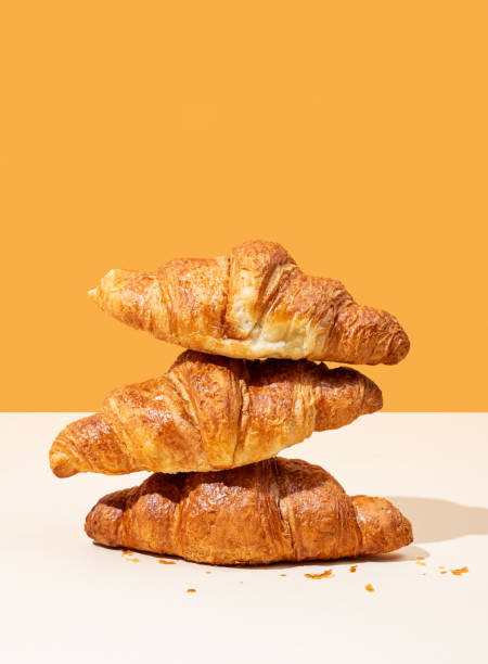 Stack of fresh croissants on yellow and orange background. Creative trendy layout and concept of healthy food or french breakfast.