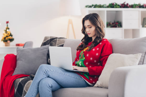 istock Photo of young concentrated programmer working stay home using her laptop chatting with boss programmer sitting sofa xmas atmosphere 2177224219