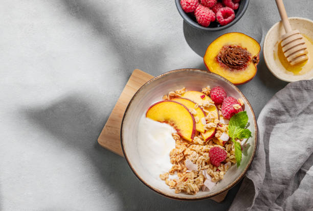 istock Natural yogurt with oat granola, peach, raspberry and honey in a bowl on a light background 2177224456