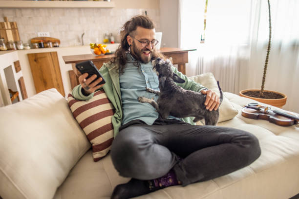 istock Man using mobile phone while relaxing with his dog at home. 2177229375