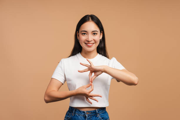 Smiling Asian woman communicating using sign language looking at camera isolated on beige background