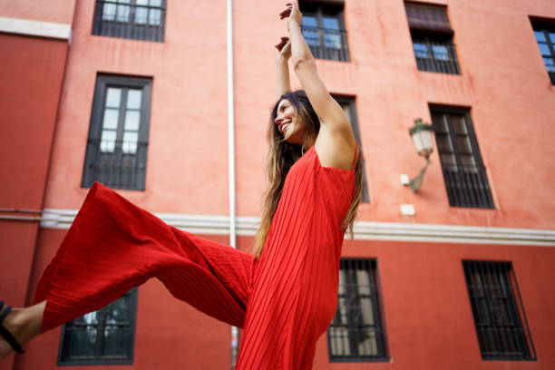 A bright, cheerful young woman joyfully dancing in a vibrant red dress set against a lively and colorful urban backdrop, radiating pure happiness and vitality with every movement she makes