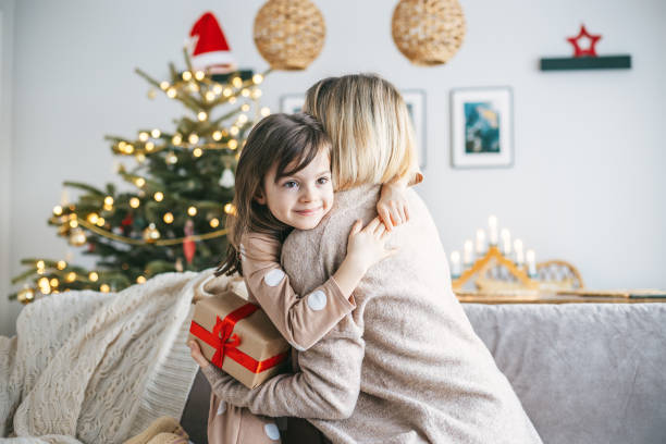istock A mother and daughter hugging while exchanging a present on a couch, the Christmas tree behind them glowing with holiday lights 2177237085