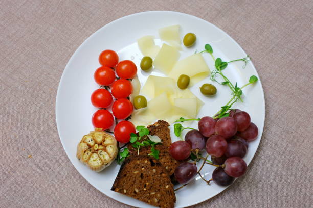 cut cheese into slices on plate with cherry tomatoes grapes and olives microgreens decoration. serving cheese in a restaurant