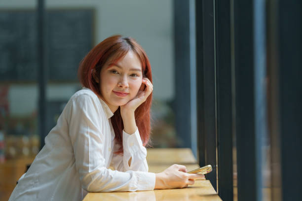 istock Asian woman holding a smartphone in her hands and smiling while looking at the camera. 2177242906