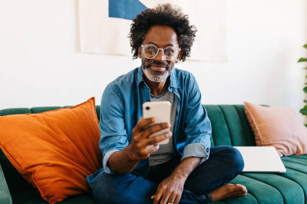 istock Man with Afro hair sitting on a couch and browsing a mobile app on his phone 2177243797