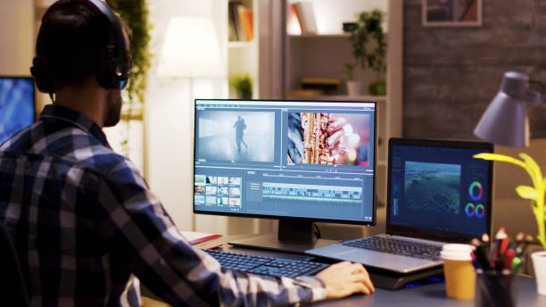 Film maker pointing at the monitor in home office Film maker pointing at the monitor in home office while working on post production for a movie. Video editor wearing headphones. photo editing screen stock pictures, royalty-free photos & images