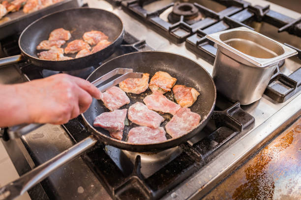 A chef expertly cooks slices of meat in a pan on a modern stove. The kitchen setting highlights culinary skills and attention to detail in preparing a delicious meal.