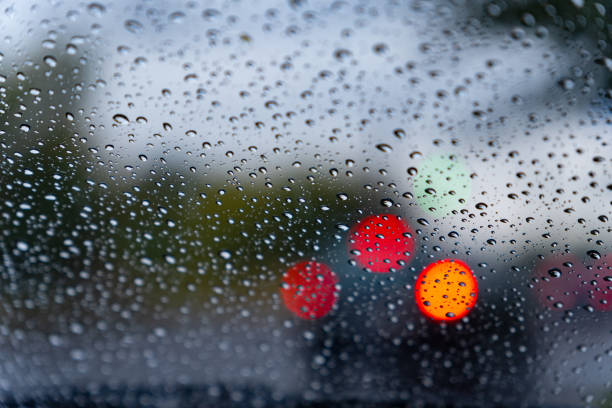 Raindrops coat a window, blurring the view of red lights from vehicles in the background, depicting a typical rainy day ambiance.