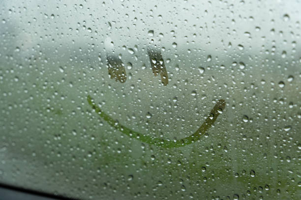istock A single, simple smiley face is drawn on a car window. The window is covered in raindrops, obscuring the view outside. The smiley face is visible through the water droplets 2177260103