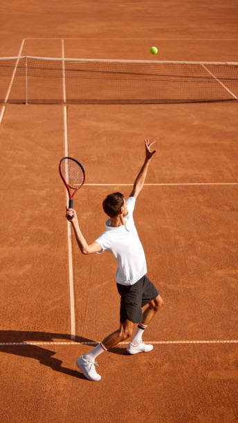 istock Vertical image of concentrated man, tennis player in uniform serving ball with racket, training on clay court. Dynamics and focus 2177264039