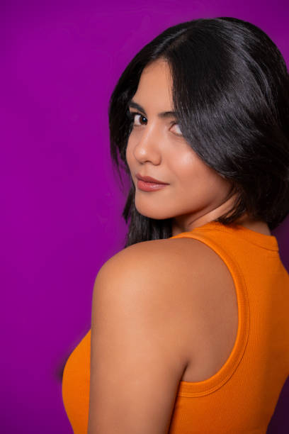 istock Confident woman in orange top looking over shoulder, vibrant purple backdrop 2177268943