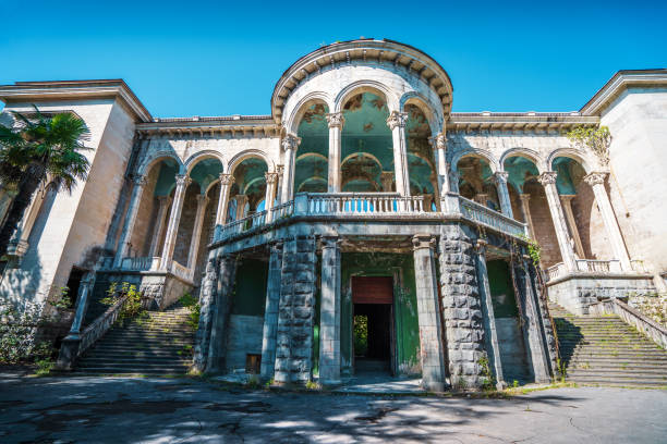 Facade of abandoned Medea sanatorium in Tskaltubo, Georgia. Neoclassical architecture with tall columns and grand arches shows signs of decay, surrounded by nature.
