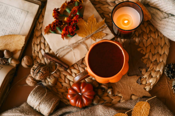 istock Cozy flat lay composition featuring an orange pumpkin-shaped mug of hot drink, a lit candle, marigold flowers, and autumn leaves on a woven surface, creating a warm and rustic autumnal mood 2177280973