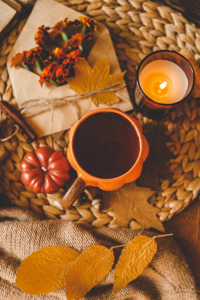 istock Cozy flat lay composition featuring an orange pumpkin-shaped mug of hot drink, a lit candle, marigold flowers, and autumn leaves on a woven surface, creating a warm and rustic autumnal mood 2177280976