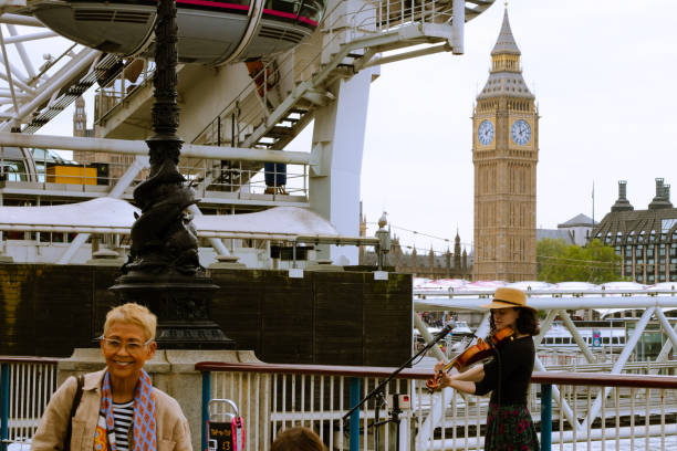 London, England, May 19 2023: Violinist playing under the London Eye with a view of the big ben in the background