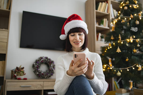 istock Woman in Santa hat using smartphone near Christmas tree 2177287712