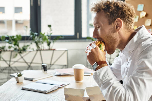 istock Redheaded businessman in white shirt enjoying a meal while working in a modern office space 2177290656
