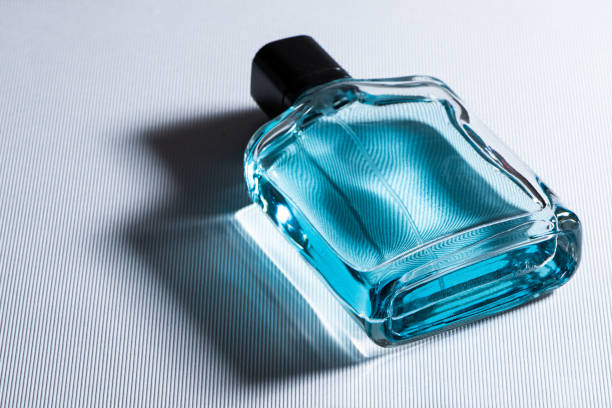 Transparent glass cosmetic perfume bottle on a blue surface. Top view