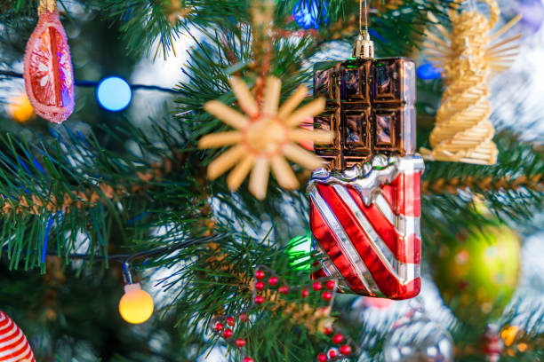 A close-up of a chocolate-shaped Christmas ornament hanging on a beautifully decorated plastic tree, surrounded by straw and glass ornaments, capturing the festive spirit and holiday cheer.