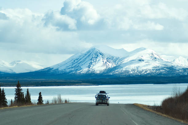 Vehicle with bicycles on road above lake and snowcapped mountains