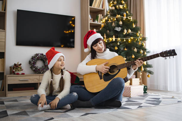 istock Mother and daughter sing Christmas carols with guitar by tree 2177298549