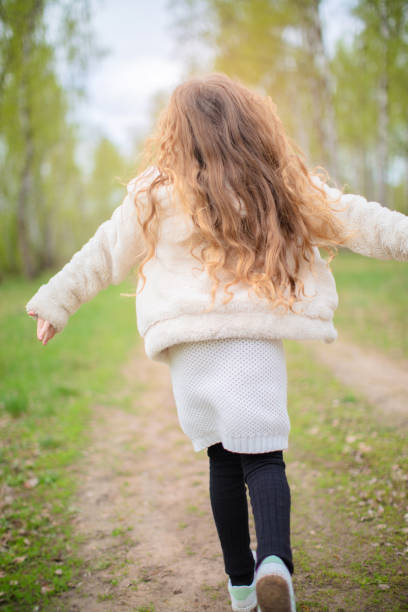A girl with long hair runs along a park path with her back to the camera.