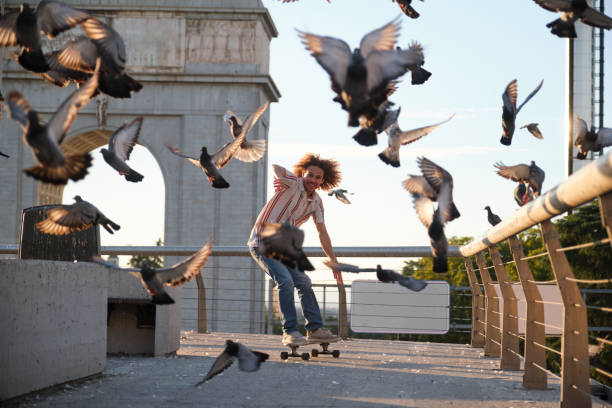istock Stylish man skateboarding in urban setting with pigeons flying around him 2177304794