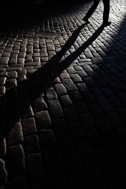 istock Shadow of walking pedestrian on cobblestone road 2177310682