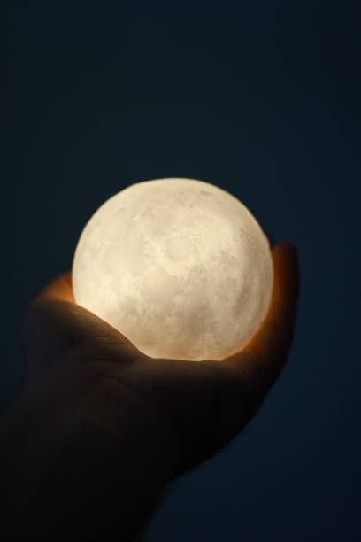 istock Hands holding an illuminated moon-like sphere lamp against a dark backdrop 2177318166