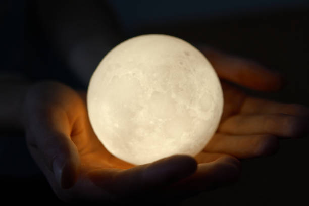 istock Hands holding an illuminated moon-like sphere lamp against a dark backdrop 2177318228