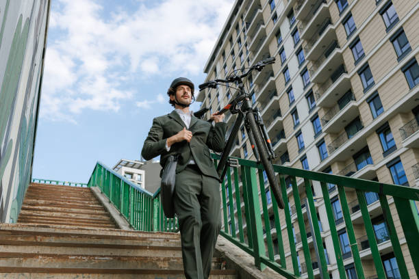 Photo of a businessman with a cycling helmet carrying his bicycle while coming down the stairs in the city, enjoying an active lifestyle.