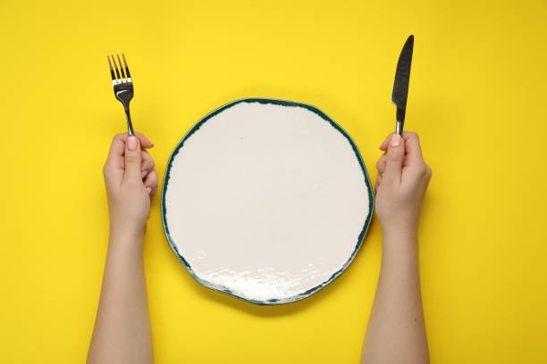 istock Woman holding fork and knife near empty plate at yellow table, top view 2177326491